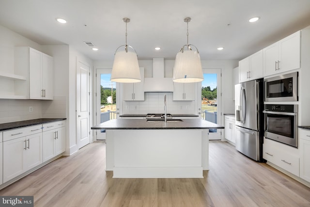 kitchen with a kitchen island with sink, hanging light fixtures, stainless steel appliances, white cabinets, and wall chimney exhaust hood