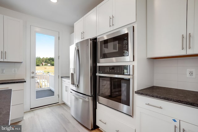 kitchen with white cabinetry, tasteful backsplash, appliances with stainless steel finishes, dark stone counters, and light hardwood / wood-style floors