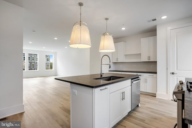 kitchen with pendant lighting, sink, appliances with stainless steel finishes, white cabinetry, and an island with sink