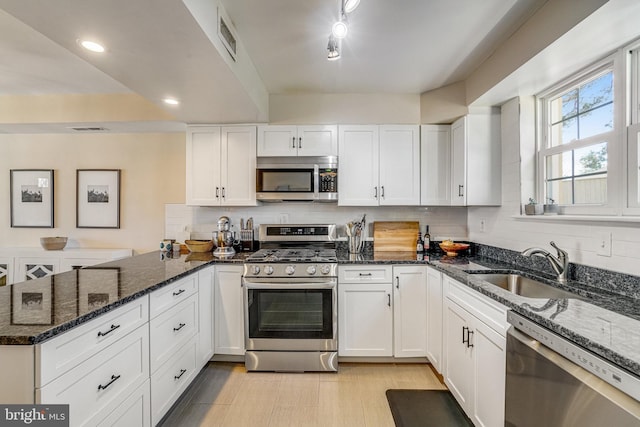 kitchen featuring white cabinetry, appliances with stainless steel finishes, and dark stone counters