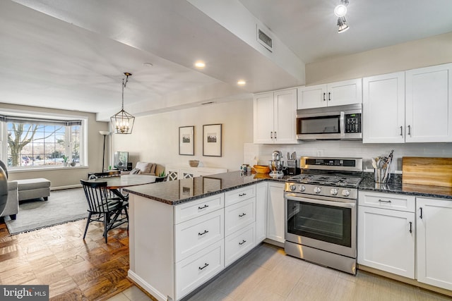 kitchen with stainless steel appliances, kitchen peninsula, dark stone counters, and white cabinets