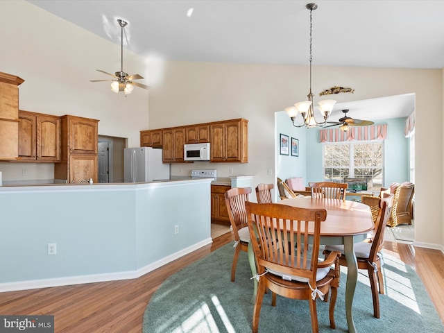 dining area featuring high vaulted ceiling, ceiling fan with notable chandelier, and light hardwood / wood-style floors