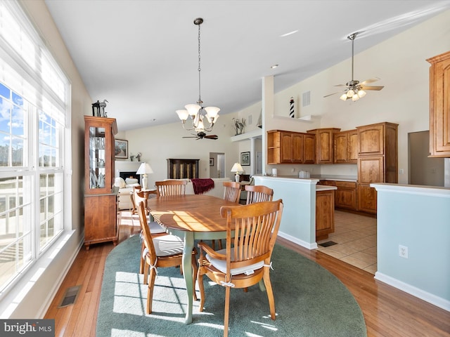 dining area featuring lofted ceiling, ceiling fan with notable chandelier, and light hardwood / wood-style floors