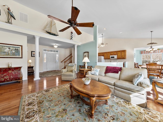 living room featuring ornate columns, hardwood / wood-style flooring, ceiling fan with notable chandelier, and high vaulted ceiling