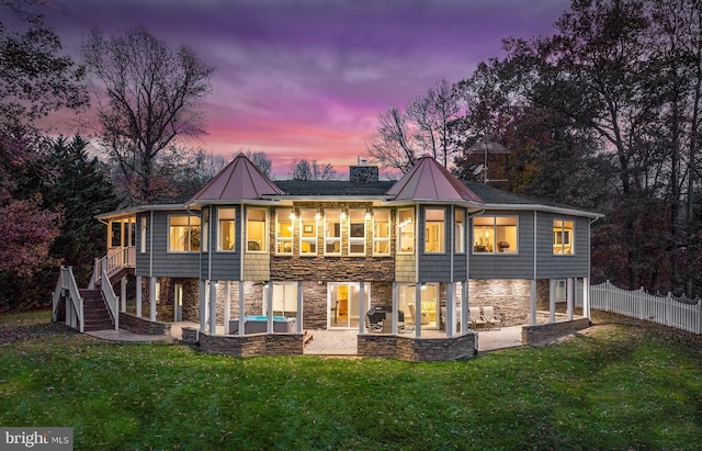 back house at dusk featuring a patio, a sunroom, and a lawn