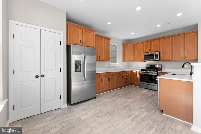 kitchen featuring brown cabinetry, light wood-style flooring, stainless steel appliances, light countertops, and a sink