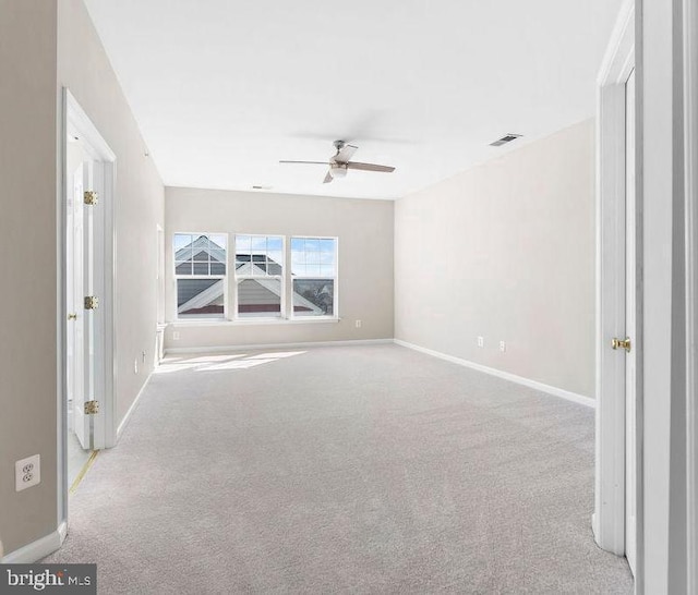 spare room featuring light colored carpet, ceiling fan, visible vents, and baseboards