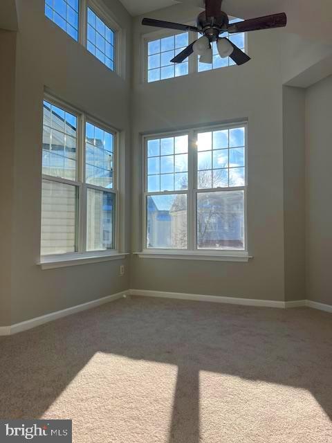 carpeted empty room featuring ceiling fan, a high ceiling, and baseboards