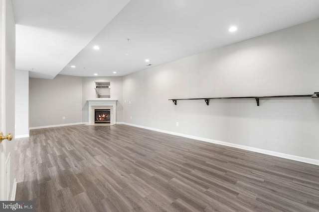 unfurnished living room featuring wood finished floors, recessed lighting, a fireplace with flush hearth, and baseboards