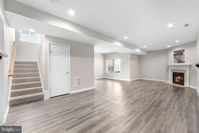 unfurnished living room with a lit fireplace, stairway, visible vents, and light wood-style floors