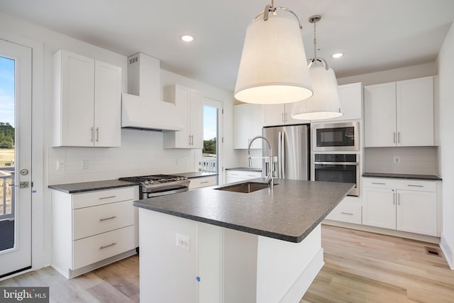 kitchen featuring decorative light fixtures, sink, a kitchen island with sink, stainless steel appliances, and wall chimney range hood