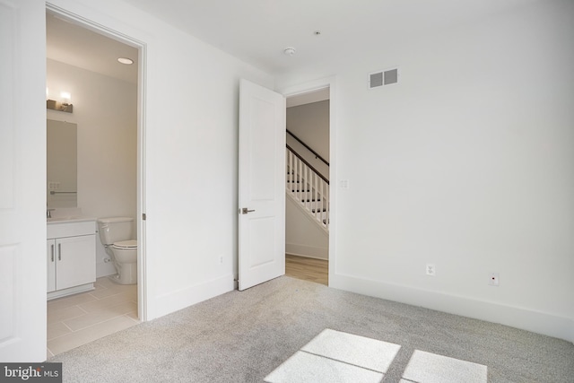 unfurnished bedroom featuring ensuite bath and light colored carpet