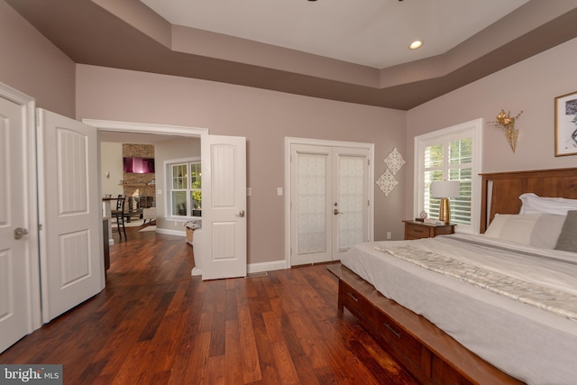 bedroom featuring dark hardwood / wood-style floors, a tray ceiling, access to exterior, and french doors