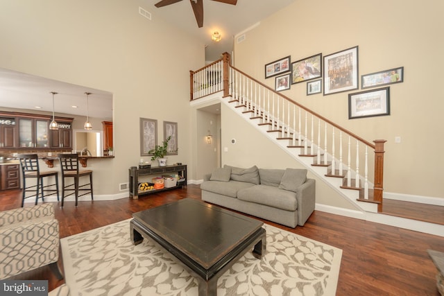 living room with dark wood-type flooring, a towering ceiling, and ceiling fan