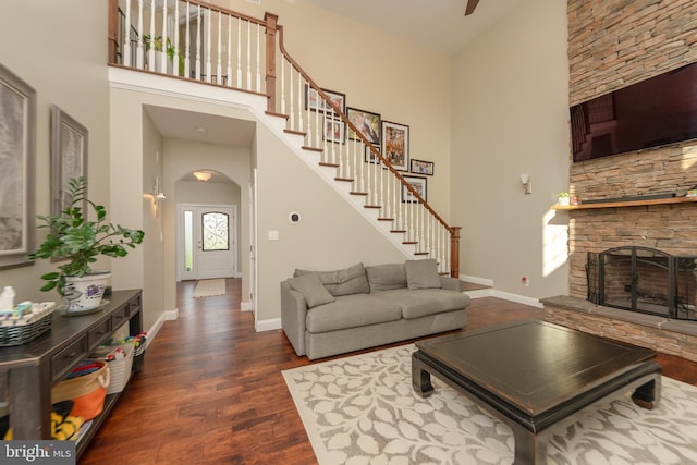 living room featuring dark wood-type flooring, a towering ceiling, and a stone fireplace