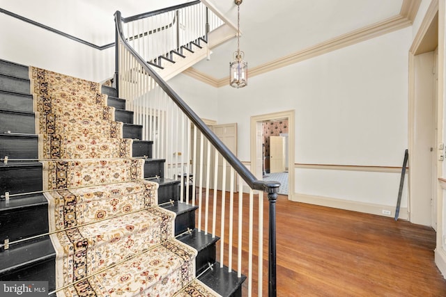 stairway with crown molding and wood-type flooring