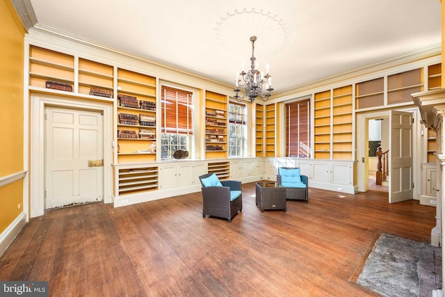 sitting room with hardwood / wood-style flooring, ornamental molding, built in features, and a chandelier