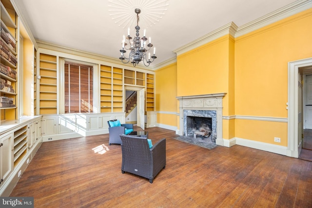 living room with ornamental molding, a notable chandelier, a high end fireplace, and built in shelves