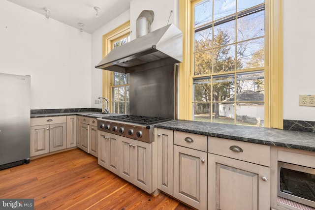 kitchen with appliances with stainless steel finishes, sink, wall chimney range hood, and light hardwood / wood-style floors