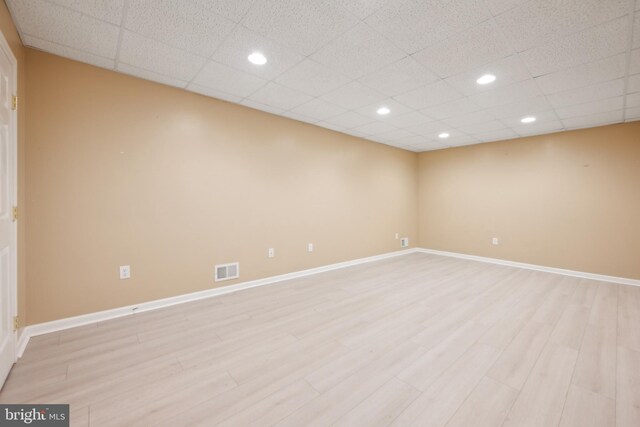spare room featuring a drop ceiling and light hardwood / wood-style flooring