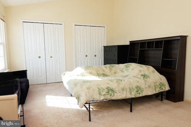 bedroom with vaulted ceiling, two closets, and light colored carpet