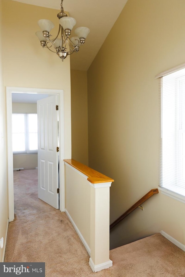 hallway featuring high vaulted ceiling, light colored carpet, and an inviting chandelier