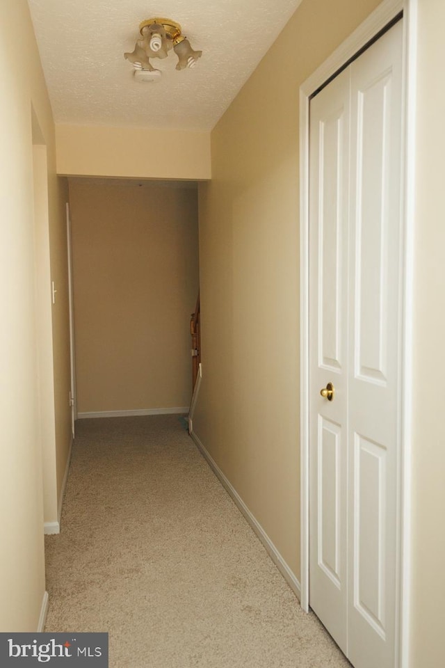 corridor with light carpet and a textured ceiling