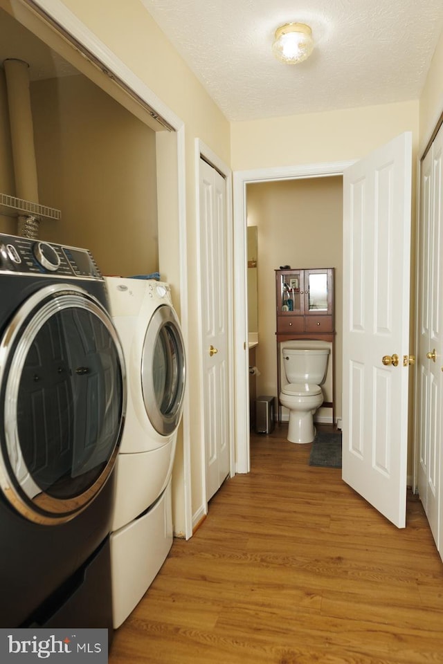 laundry area with independent washer and dryer, a textured ceiling, and light wood-type flooring