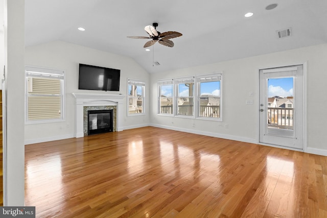 unfurnished living room featuring lofted ceiling, a premium fireplace, plenty of natural light, and light wood-style flooring