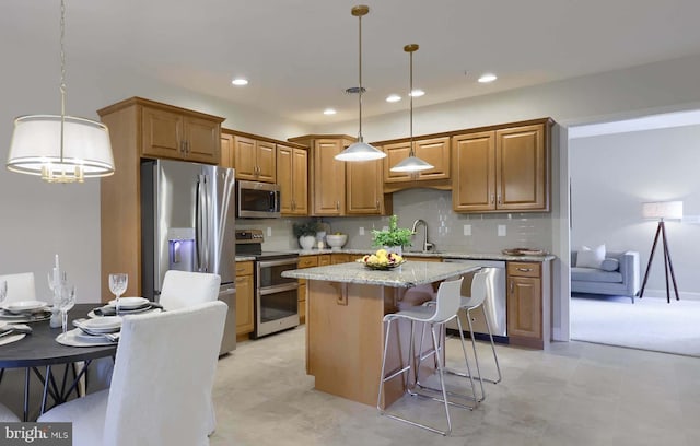 kitchen with appliances with stainless steel finishes, hanging light fixtures, a center island, light stone countertops, and a kitchen bar