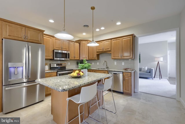 kitchen featuring light stone counters, hanging light fixtures, appliances with stainless steel finishes, a kitchen island, and decorative backsplash