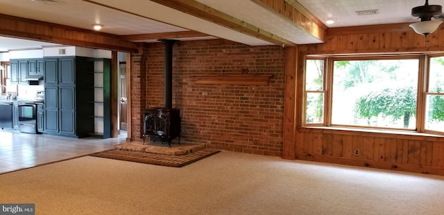 unfurnished living room featuring wooden walls, light colored carpet, brick wall, and a wood stove