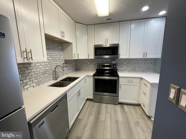 kitchen featuring sink, light hardwood / wood-style flooring, appliances with stainless steel finishes, white cabinetry, and tasteful backsplash