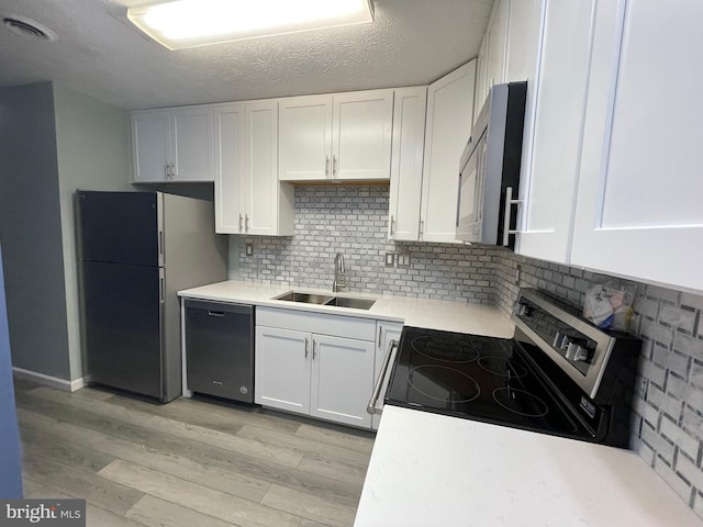 kitchen featuring sink, appliances with stainless steel finishes, white cabinetry, decorative backsplash, and light wood-type flooring