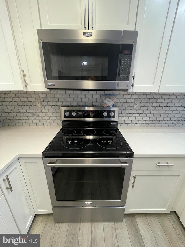 kitchen featuring white cabinetry, appliances with stainless steel finishes, light hardwood / wood-style floors, and backsplash