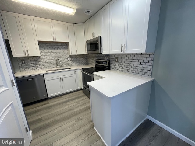 kitchen featuring tasteful backsplash, white cabinetry, sink, light hardwood / wood-style floors, and stainless steel appliances