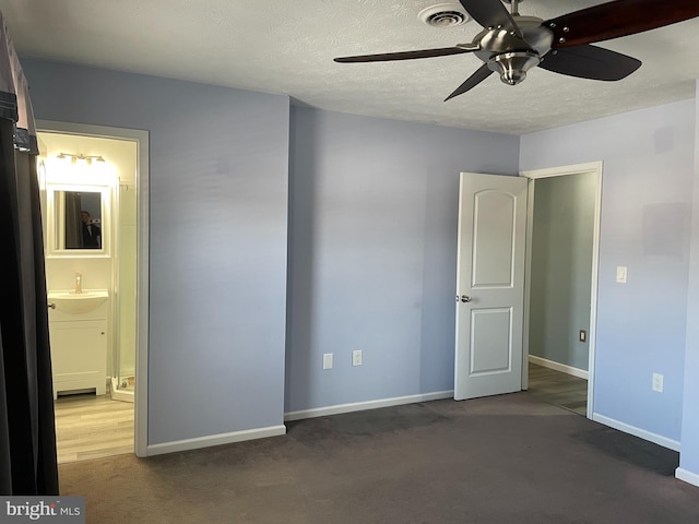 unfurnished bedroom with ensuite bath, sink, dark carpet, ceiling fan, and a textured ceiling