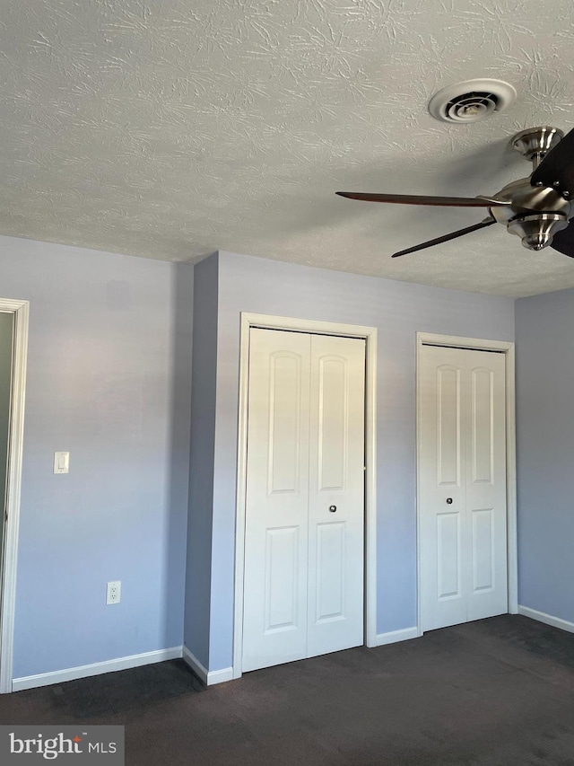 unfurnished bedroom with dark carpet, two closets, and ceiling fan