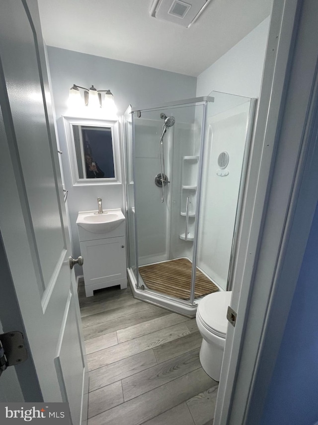 bathroom with vanity, hardwood / wood-style flooring, a shower with door, and toilet