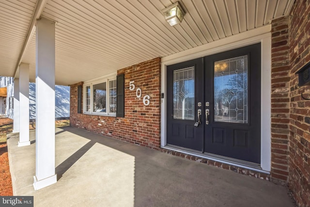 entrance to property with french doors, brick siding, and a porch