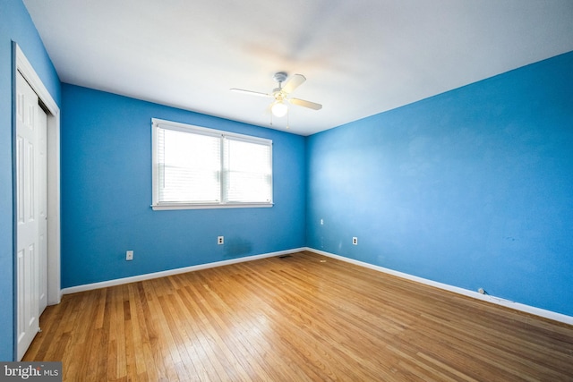 unfurnished bedroom with a closet, a ceiling fan, baseboards, and hardwood / wood-style floors