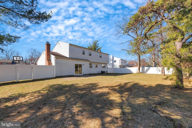 back of house featuring central AC unit, a fenced backyard, a lawn, and a chimney