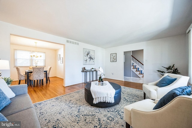 living area with visible vents, an inviting chandelier, wood finished floors, and stairs