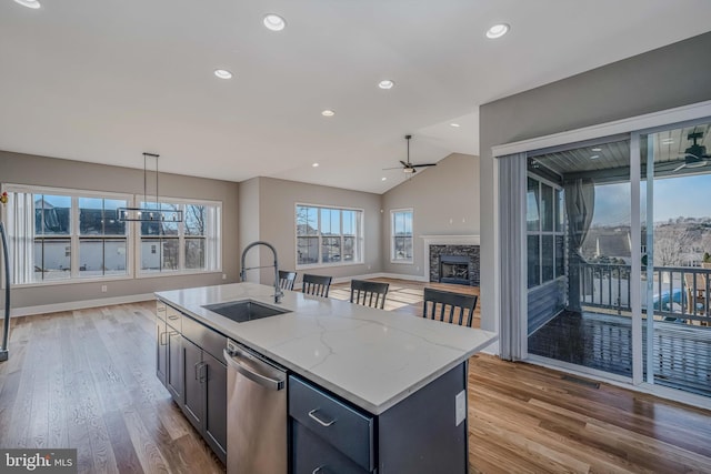 kitchen with sink, a kitchen island with sink, hanging light fixtures, light stone countertops, and stainless steel dishwasher