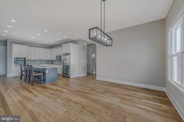 kitchen with a breakfast bar area, appliances with stainless steel finishes, a center island, white cabinets, and decorative light fixtures