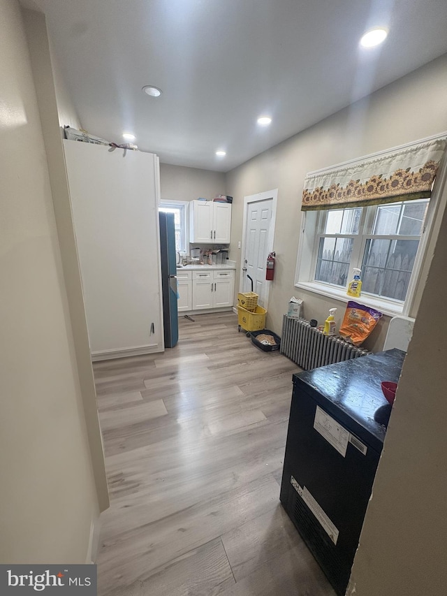 kitchen with white cabinetry, black refrigerator, and light hardwood / wood-style floors