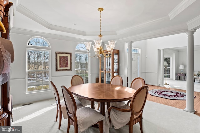 dining area with ornate columns, a raised ceiling, and a notable chandelier