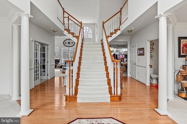 staircase with hardwood / wood-style flooring, a towering ceiling, and decorative columns