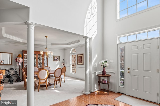 foyer entrance featuring an inviting chandelier, crown molding, light hardwood / wood-style flooring, and decorative columns