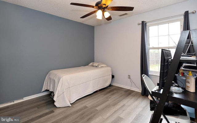 bedroom with ceiling fan, wood-type flooring, and a textured ceiling